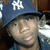 A pixelated close-up of a person wearing a dark blue cap with white 'NY' lettering, partially visible face, and dark clothing against a blurred background.