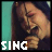 six pixelated frames showing a person with long dark hair against a teal background, each frame displaying the word "SING" in different colors