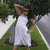 A pixelated image shows a person in a white dress standing outdoors with greenery and blurred background elements.