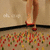 A pixelated image shows a person's lower legs and feet in red shoes stepping on colorful scattered objects against a beige background with faint cloud shapes.