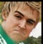 Pixelated close-up of a person with light brown hair, green shirt, and neutral expression against blurred background.