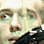 Pixelated close-up of a person's face showing eyes, nose, and mouth with light skin tone and dark hair, wearing a dark shirt.