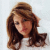Pixelated static image of a person with long brown hair, light skin tone, and dark eyes wearing a white top against a plain light background.