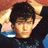 Pixelated image of a person with dark hair wearing a dark shirt with blue accents, hands behind head, next to yellow text on black background.