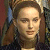 Static pixelated image of a person with light skin tone, brown hair styled in an updo, wearing dark clothing and large earrings against a blurred background.
