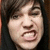 Pixelated close-up of a person's face with dark hair, showing an open mouth and squinted eyes against a dark background.