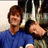 Two people in a close pose, one wearing blue shirt with brown hair and the other resting head on shoulder.