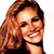 Pixelated close-up of a smiling person with long wavy brown hair wearing a dark top against a white background.