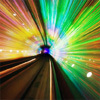 A blurred, colorful tunnel with radiating light beams in green, yellow, and blue, featuring a dark central structure with a purple glow at the end.