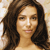 Pixelated close-up of a person with long dark brown hair, light skin tone, and neutral expression against a light beige background.