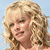 Pixelated close-up of a person with voluminous curly blonde hair against a light blue background, showing partial facial features and a neutral expression.
