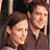 Two pixelated human faces in close proximity, one with short dark hair and the other with light hair, both rendered in warm brown and beige tones against a dark background.