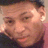 Pixelated close-up of a person's face with light skin tone, visible eyes, nose, mouth, and ear, set against a blurred background with pink and dark tones.