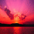 Pixelated sunset scene with orange and pink sky reflecting on water, dark silhouette of landmass at horizon.