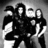 Black-and-white pixelated image of four figures in dark clothing with white accents, standing closely together against a gradient background.