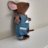 Pixelated cartoon mouse in blue overalls with brown body and pink ears, standing against light gray background.