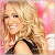 A pixelated close-up of a smiling person with long blonde hair wearing a black strap top against a pink and white background.