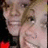 Pixelated close-up of a person with light brown hair, smiling broadly showing teeth, wearing dark clothing and holding a red object.