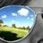 Pixelated landscape icon showing blue sky with white clouds, green and yellow fields, distant dark structures on horizon.