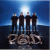 Five figures in black clothing stand in a on a dark platform beneath a bright blue background, with '2000' text below them