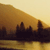 Pixelated landscape with dark silhouetted structures against a gradient sky transitioning from deep brown to pale yellow, reflecting in a lower water-like surface.
