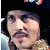 Pixelated close-up of a person with dark hair, mustache, and light skin tone, wearing a dark jacket over a light shirt, against a dark background with faint blue and white elements.
