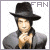 Pixelated image of a person wearing a black wide-brimmed hat and gray jacket, with hands clasped near the chest against a white background.