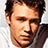 Pixelated image of a person with short brown hair and light skin, wearing a white shirt against a bright blue background.