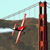 Pixelated image of a red and white figure in mid-air near a tall brown structure with orange accents against a light blue sky and brown terrain.