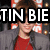 A pixelated image of a person in a red shirt and gray jacket with text overlays reading "TIN BIE WANTS TONS D" across the top and bottom sections.