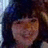 Pixelated close-up of a person with dark hair and light skin, wearing a dark top against a blurred background.