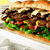 Pixelated image of a sandwich with visible layers of meat, lettuce, tomato, and cheese on a light-colored surface.