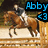 Pixelated image of a person riding a brown horse on a light-colored surface with a wooden fence and dark background.