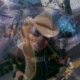 Animated sequence of a person wearing a straw cowboy hat, dark sunglasses, and a dark jacket with orange trim against a blurred outdoor background.