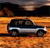 A pixelated black SUV with a silver stripe on its side is positioned on a textured orange-brown surface, with a dark background above.