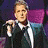 Four distinct views of a person in formal attire: top-left shows the figure holding a microphone against purple and blue background, top-right is a close-up with dark hair on white surface, bottom-left features the person looking downward with brown backdrop, bottom-right displays 'CROONER' text below the figure.