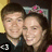 Two people stand side-by-side; the person on the right wears a pink bow and has a purple heart symbol over their chest.
