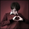 A person in a red and black striped sweater forms a heart shape with their hands against a solid maroon background.