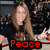 A woman with long brown hair in a black top makes hand gestures against a blurred crowd background, with red text labels appearing below her.
