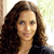 A pixelated portrait of a person with long dark brown hair, light skin, and a neutral expression, wearing a dark top against a light background.