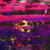 Pixelated image with dominant pink and purple hues, featuring a central yellowish shape against a dark background with scattered red and blue pixels.