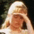 A pixelated image of a blonde woman with her hand on her forehead, set against an orange background with green text.