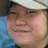 Pixelated image of a person wearing a light-colored cap and blue clothing on a light green background with orange text.