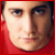 Pixelated close-up of a person's face with light skin, dark eyes, and brown hair against a red background.