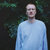Pixelated static image of a person in a light blue long-sleeve shirt against a dark green background with visible pixelation and low resolution.