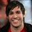 A pixelated close-up of a person with dark hair wearing a red and black garment against a light blue background.