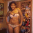 A pixelated static image shows a person in a yellow bikini top and white bottoms standing in front of a wooden background with shelves holding various items.