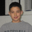 Pixelated static image of a person with short dark hair wearing a gray shirt against a light background with dark vertical elements.