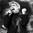 Pixelated grayscale image of a figure in dark clothing holding a microphone, with a blurred background and visible pixelation artifacts.