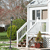 Static pixelated image of a white house with multiple windows, green trees, and a red object near the base, set against a blurred background.